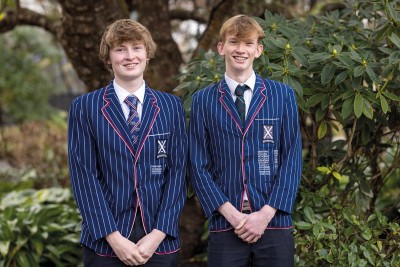 Luke and Tom stand in front of trees in their uniforms smiling for a photo