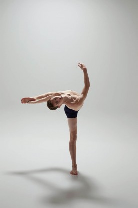 Joshua performs a back bend and leg extension in front of a plain white photography studio background.