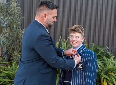 Head of Boarding, Matt Parr puts new badge on boarding student, James', blazer. The two stand outside.