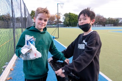 Two boys from the Preparatory School stand on the turf with a rubbish bag and rubbish as they participate in their eco day.