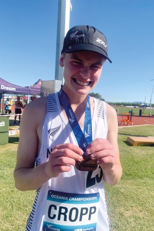 Jonah smiles for photo in his New Zealand Representative uniform, with the bronze medal he won around his neck as he holds it in front of him.