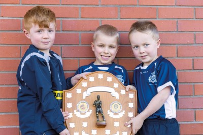 Three Preparatory School rugby players hold the rugby shield in front of a brick wall.