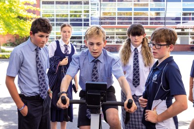 Students cheer on their peer as they cycle on a stationary bike as part of the One Human Race Challenge.