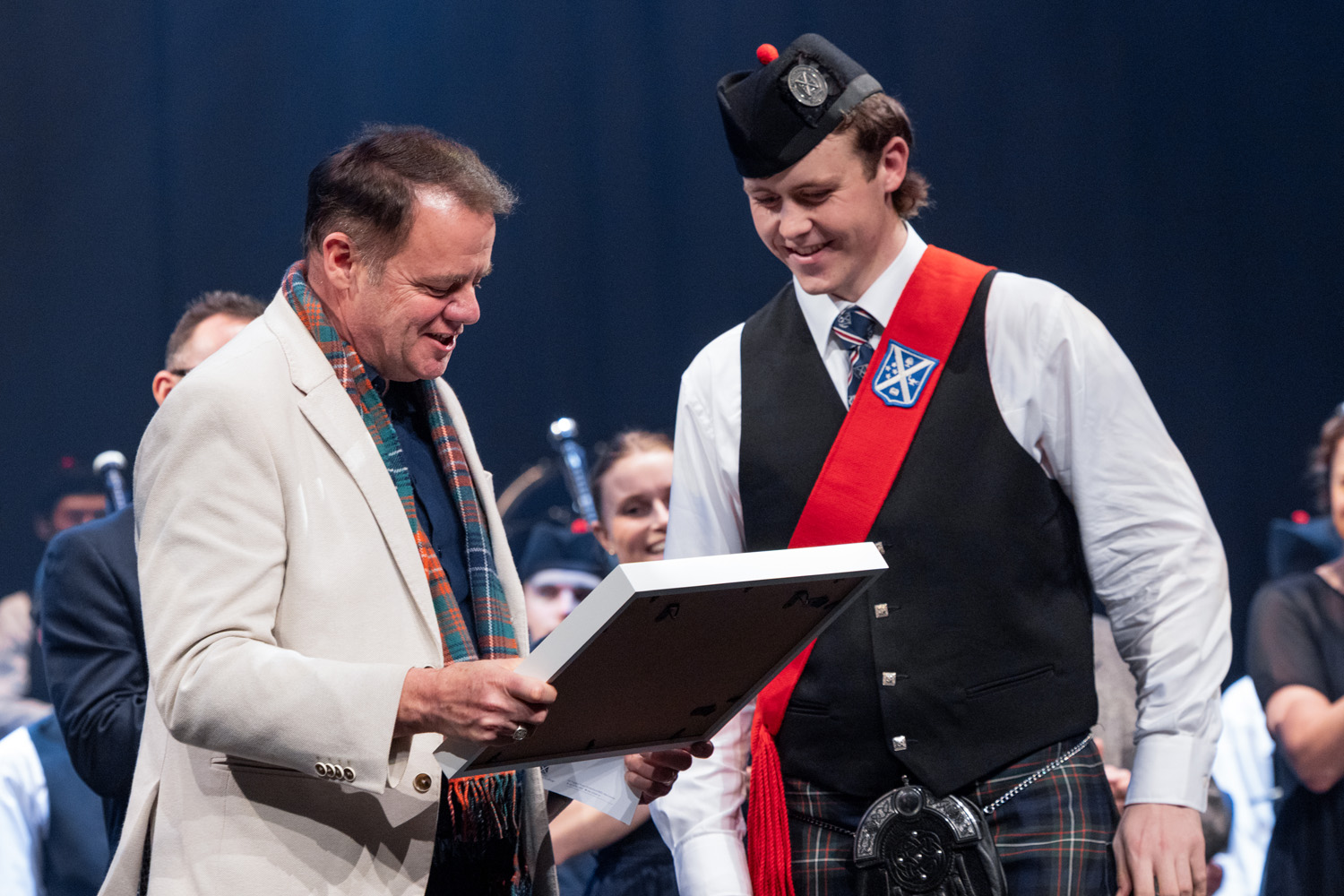 Rector, Mark Wilson, surprised by Pipe Major, Sam Foote, with framed music of a special 2/4 March tune called 'Mr Mark Wilson’s Welcome to St Andrew’s College'.