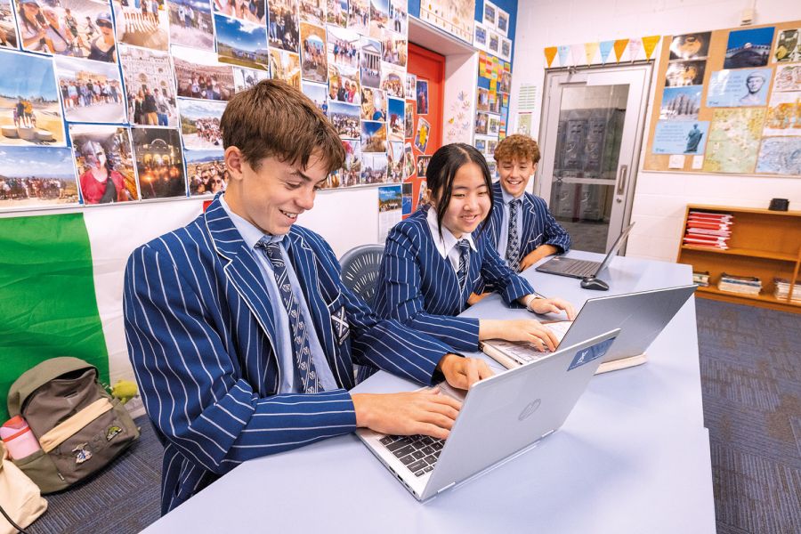 Three St Andrew's College students looking at their laptops smiling.