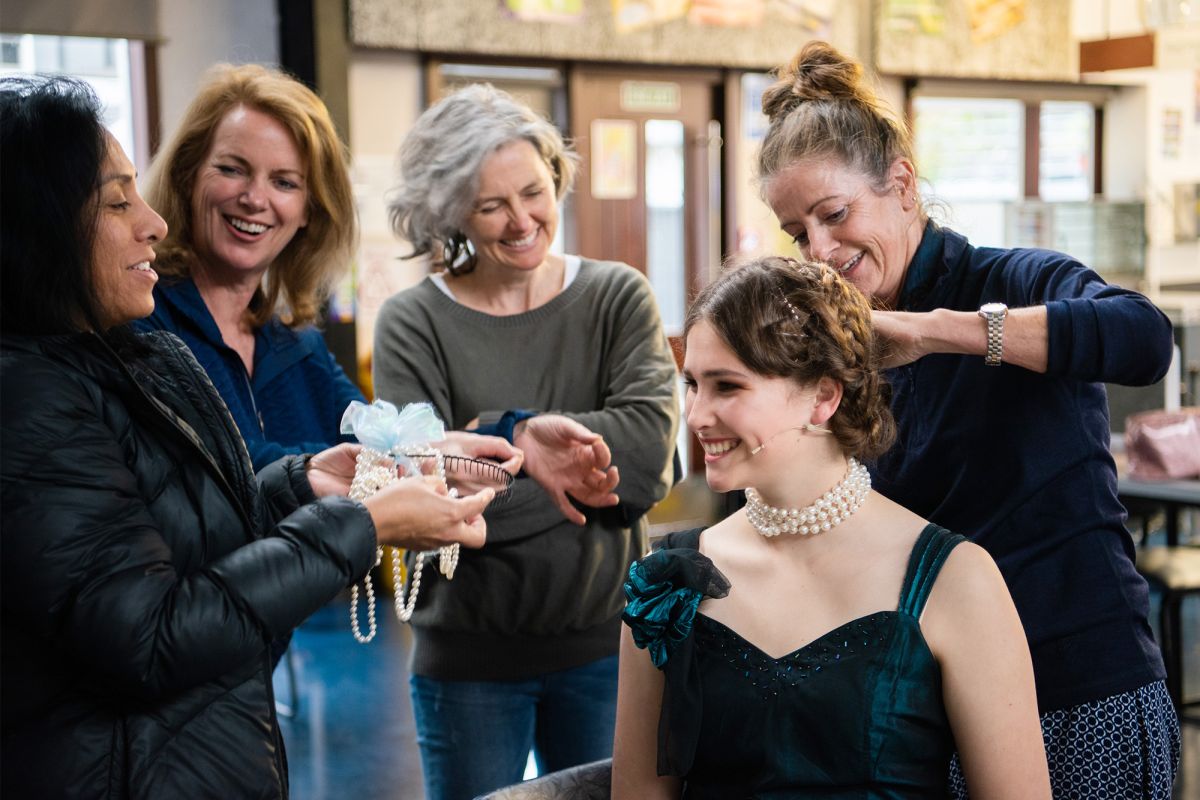 Parent volunteers help students with makeup and hair before production.