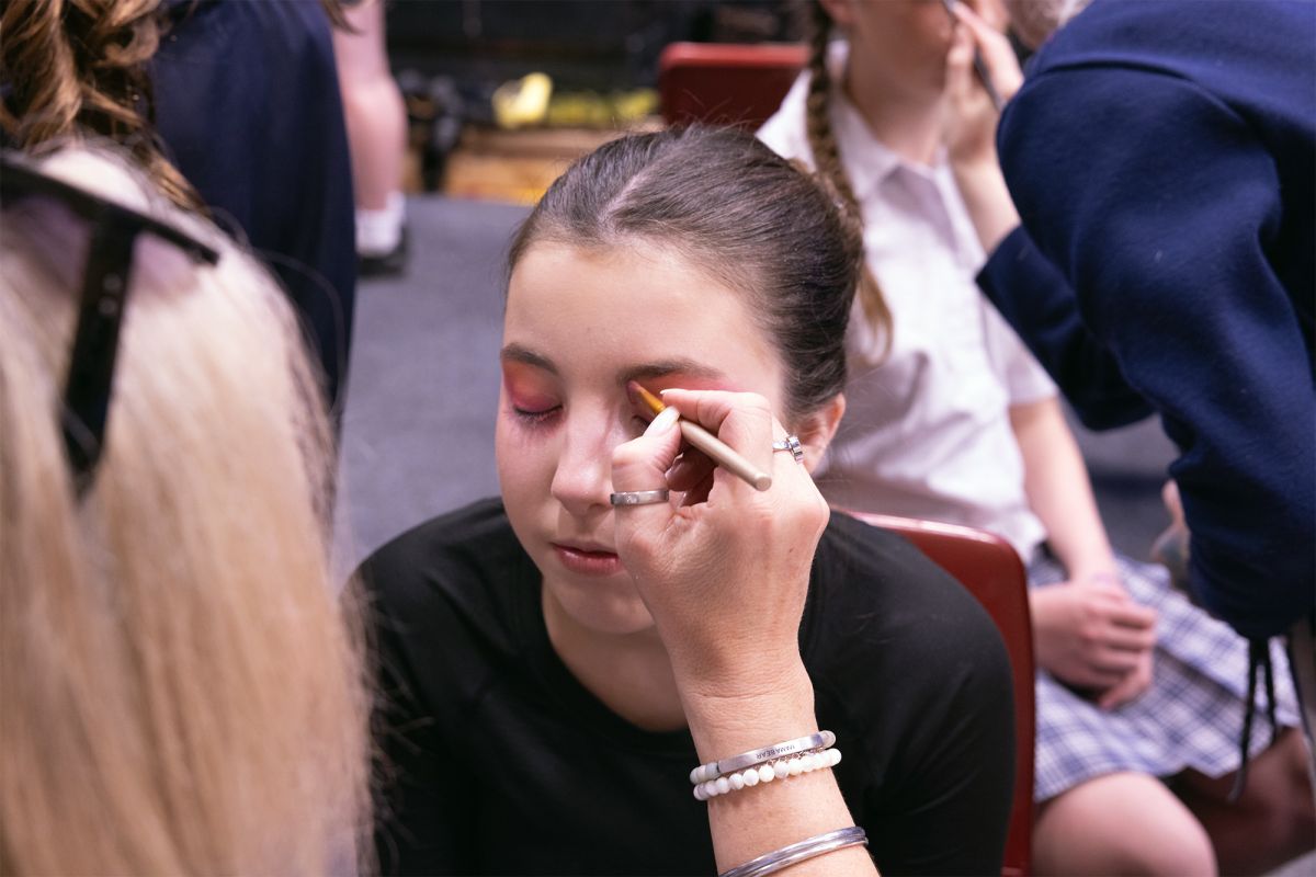 A volunteer putting makeup on a student for production.