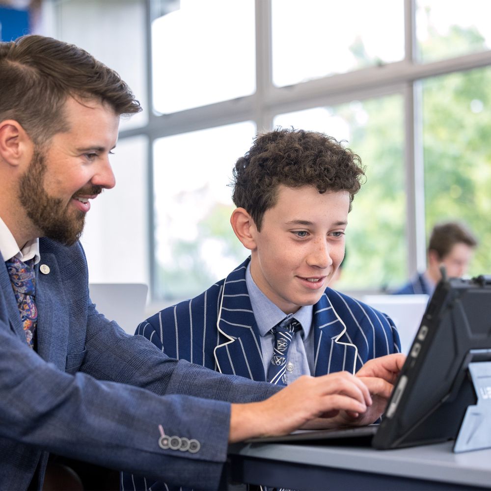Teacher and student working on a laptop in class.