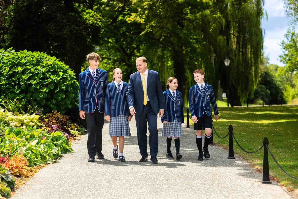 St Andrew's College Rector, Mark Wilson walking and chatting at campus with four students.