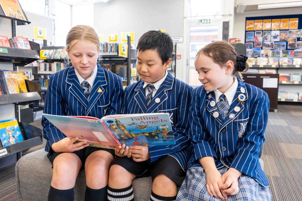 Three St Andrew's College Preparatory School students reading a book