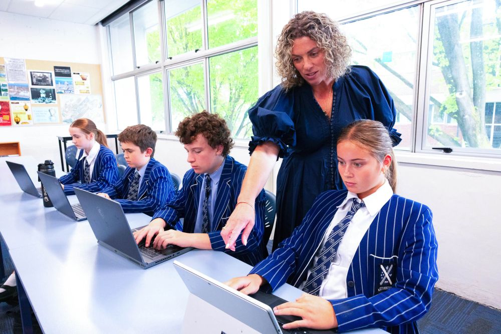 Teacher in classroom with students in uniform working on laptops