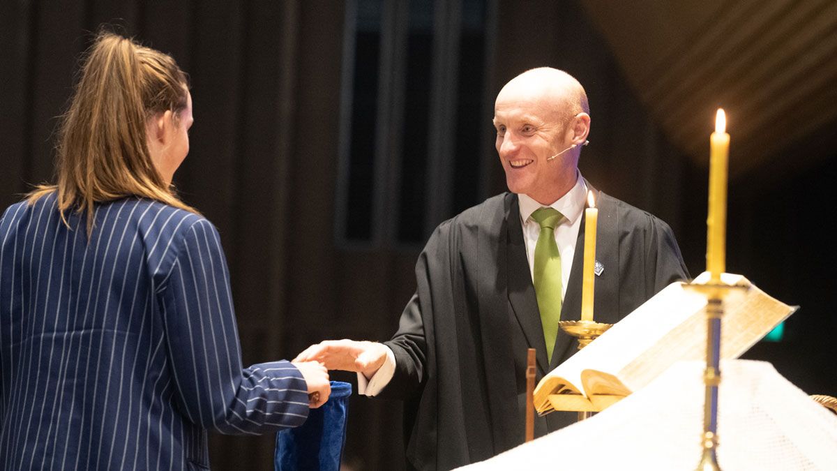 Chaplain in chapel with student holding offering pouch