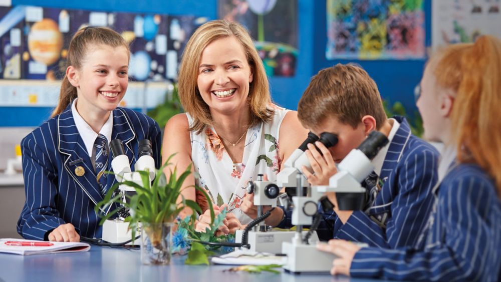 Students in science lab talking to teacher with microscopes
